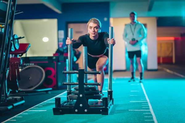 Member pushing a sled on the HYROX turf track at M Club gym